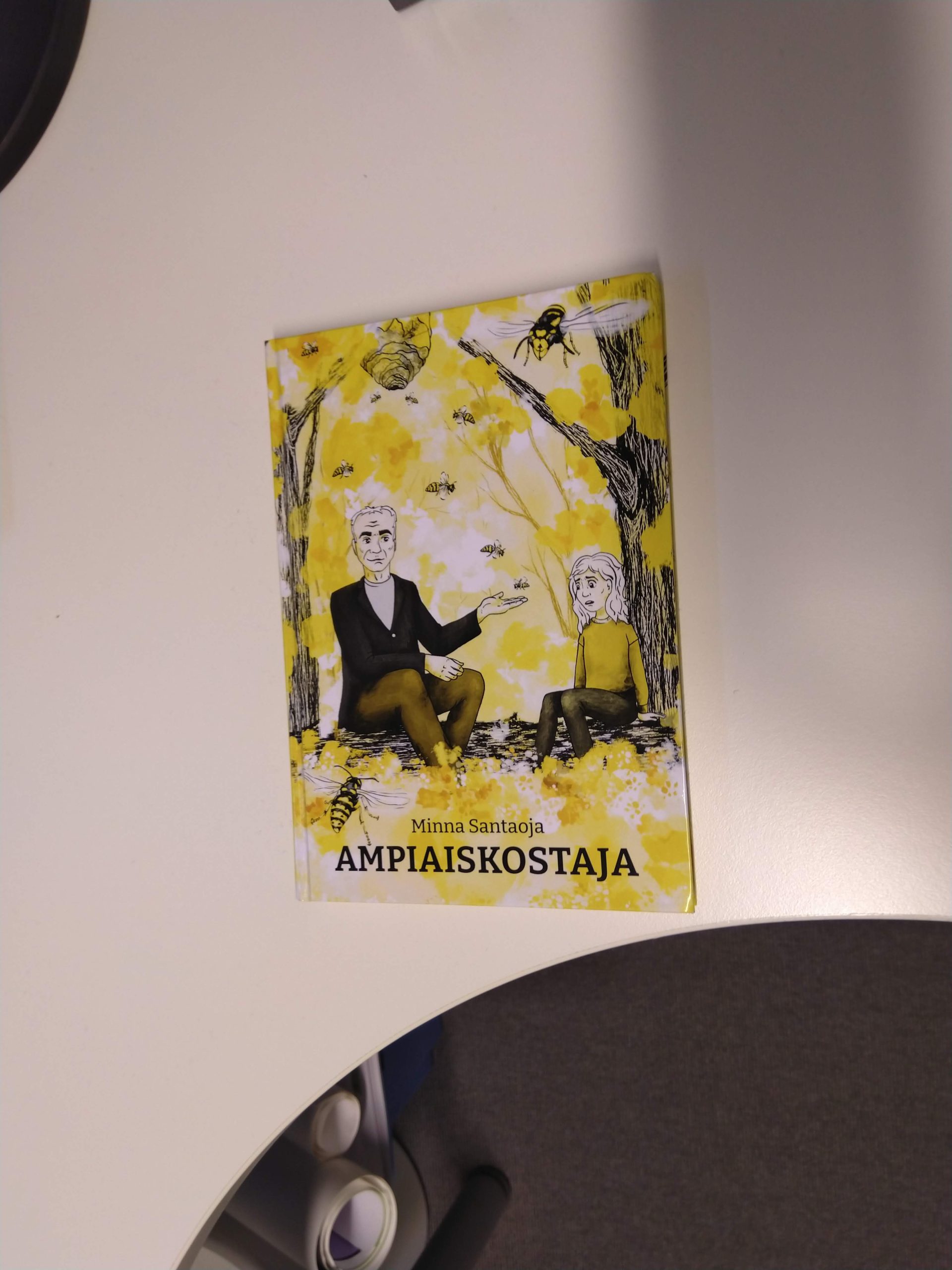 Kirjassa on keltainen kansi, jossa piirretty mies ja tyttö istuvat puun rungon alla. Heidän ympärillään lentää ampiaisia. Tyttö näyttää huolestuneelta, mies rennolta, ja on selittämässä jotain tytölle. Kannessa lukee Minna Santaoja - Ampiaiskostaja.