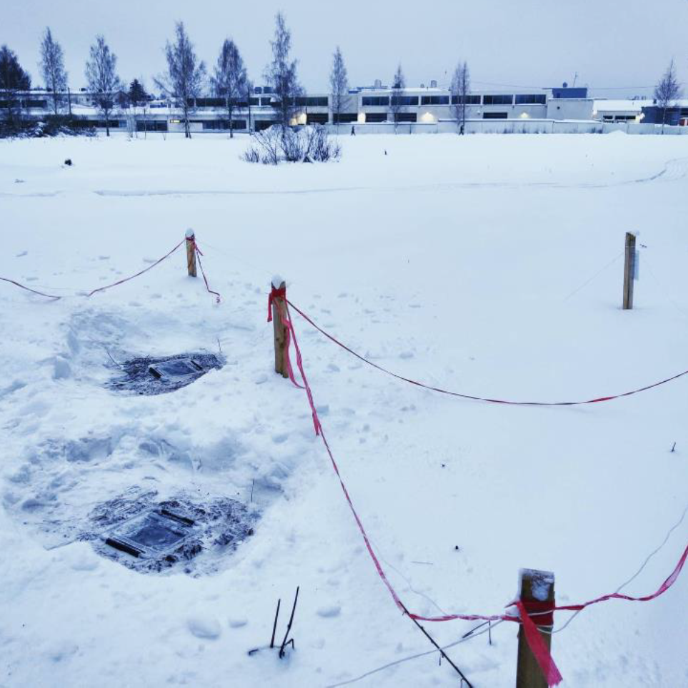 Kuvituskuva. Lumihangessa on narulla eristettyjä alueita. Lumihankea on myös kaivettu, mikä paljastaa maahan haudatut laatikot.